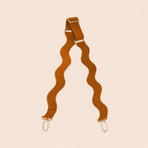Brown bag strap with gold hardware on a beige background