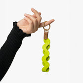 Hand holding a green wavy keychain with a brown leather strap against a white background