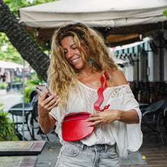 Happy woman looking at phone wearing red crossbody