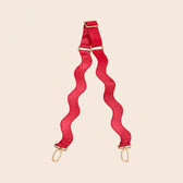 Red bag strap with gold hardware on a beige background