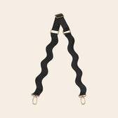 Black bag strap with gold hardware on a beige background