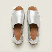 Pair of silver shoes with brown soles on a light beige background