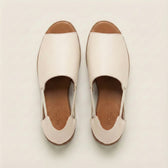 Pair of white sandals with brown soles on a light beige background