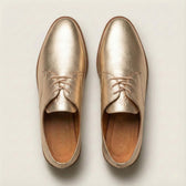 Pair of gold leather shoes on a light beige background