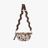 Cow print crossbody bag with brown strap on a white background