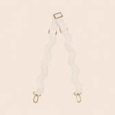 White bag strap with gold hardware on a beige background