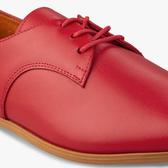 Red leather shoe with a brown sole on a white background