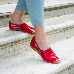 Red sandals worn on a person's feet standing on stone steps.